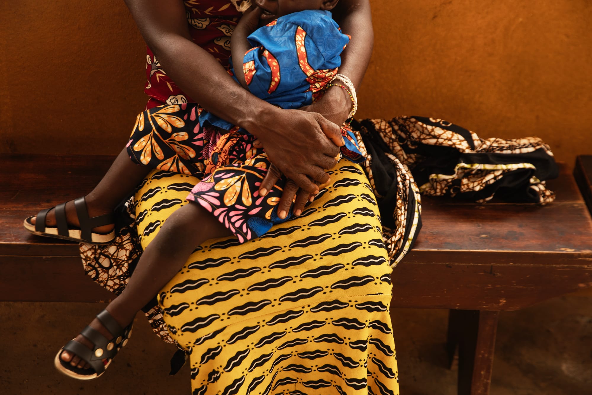 A mother with a yellow and black skirt holds her young child in her lap.