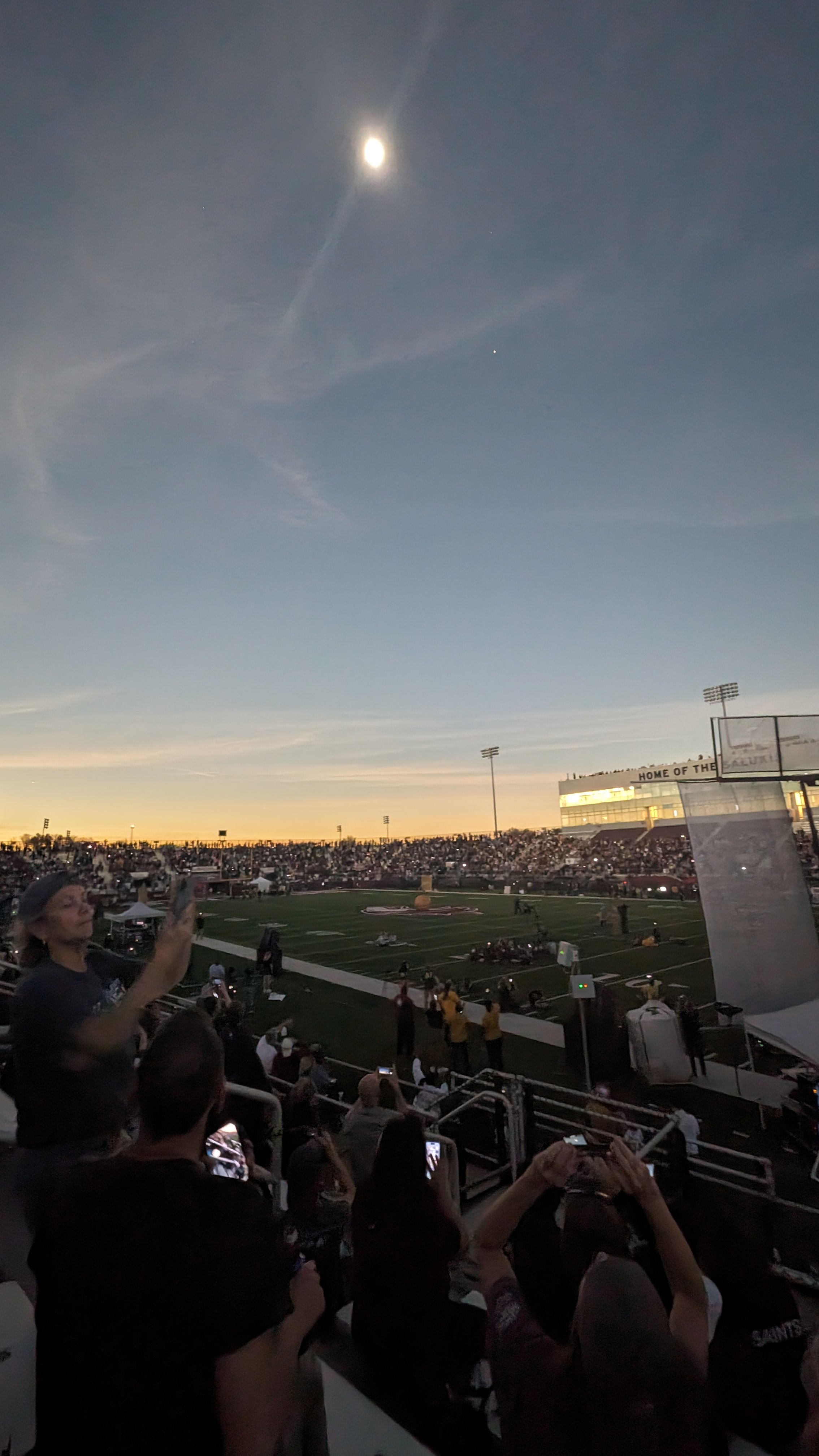 Eclipse watchers in a football stadium pointing their phone cameras skyward