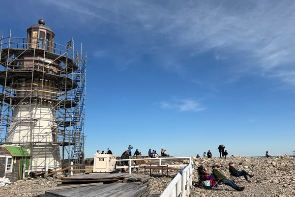 Solar eclipse watchers sitting in chairs on a rocky shore next to a lighthouse