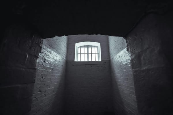 The insides of a prison cell, with a single a barred window